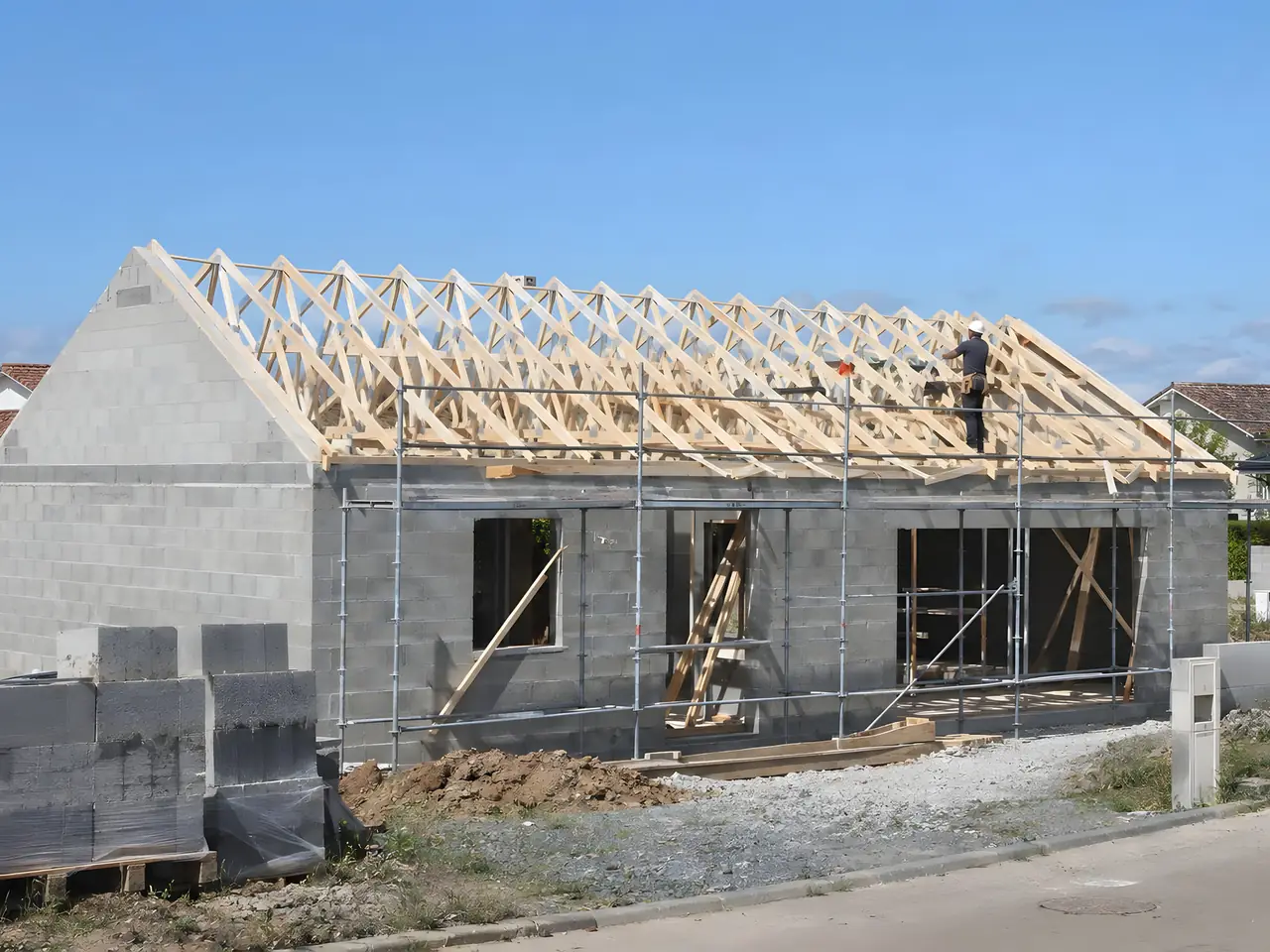 Fermettes neuves posées sur une maison en parpaings, un charpentier debout sur le toit